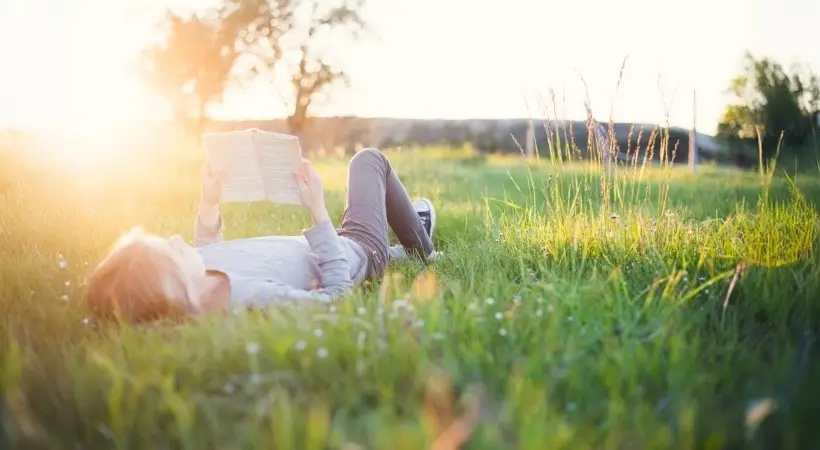 Young person lying in grass reading book at sunset 